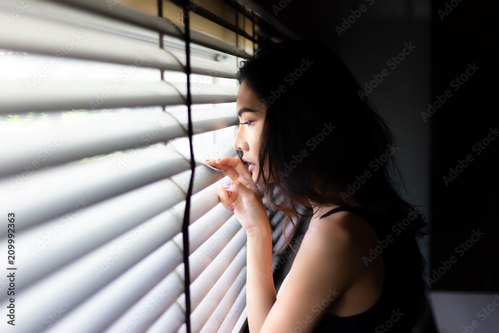 Attractive beautiful woman look through window outside house. Charming beautiful girl is waiting her husband or boyfriend for coming back to home because she gets worried about him that come too late.