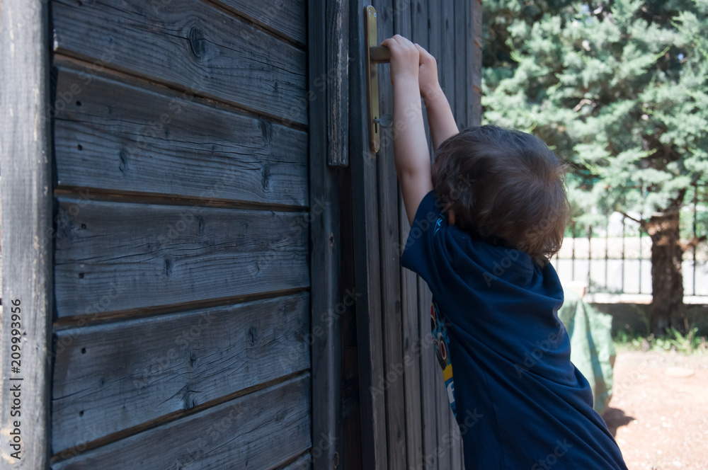 Bambino piccolo cerca di aprire la porta fuori nel giardino Bambino piccolo cerca di aprire la porta fuori nel giardino