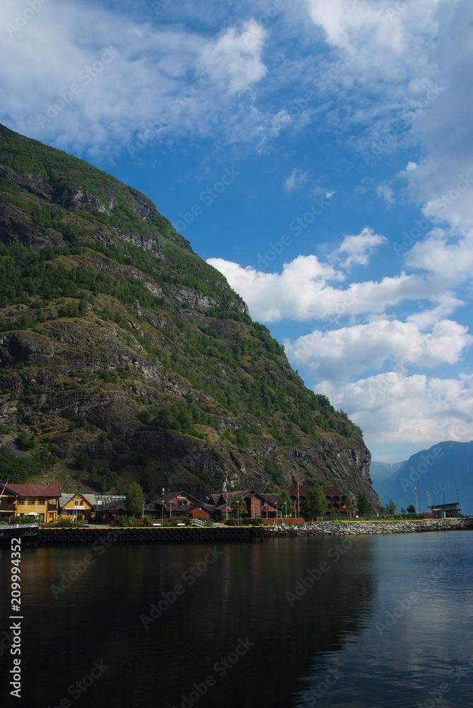 Village in Flam, Norway. Country houses at sea shore on mountain landscape. Fjord and mountains on cloudy sky. Vacation and wanderlust. Travelling and discovery