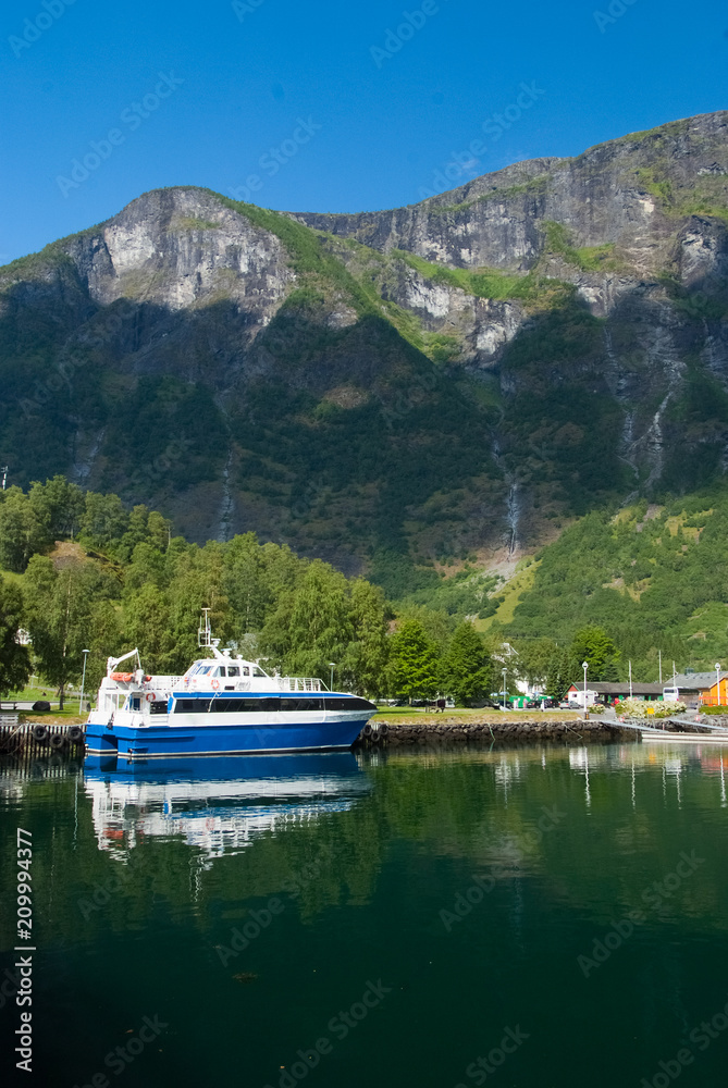 Pleasure boat at sea pier on mountain landscape in Flam, Norway. Small ship in sea harbor with green mountains. Travelling by water. Summer vacation and holiday. Wanderlust and discovery