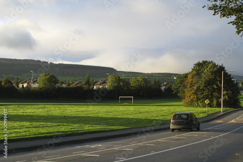 green fields in the Irish countryside, road, black car driving past the village