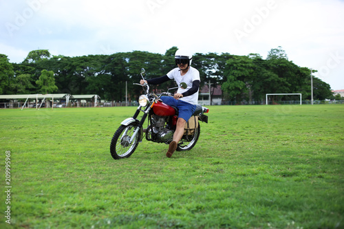 Biker men riding vintage enduro motorcycle on the grass excited and fun lifestyle. Asian rider with classic motorbike.
