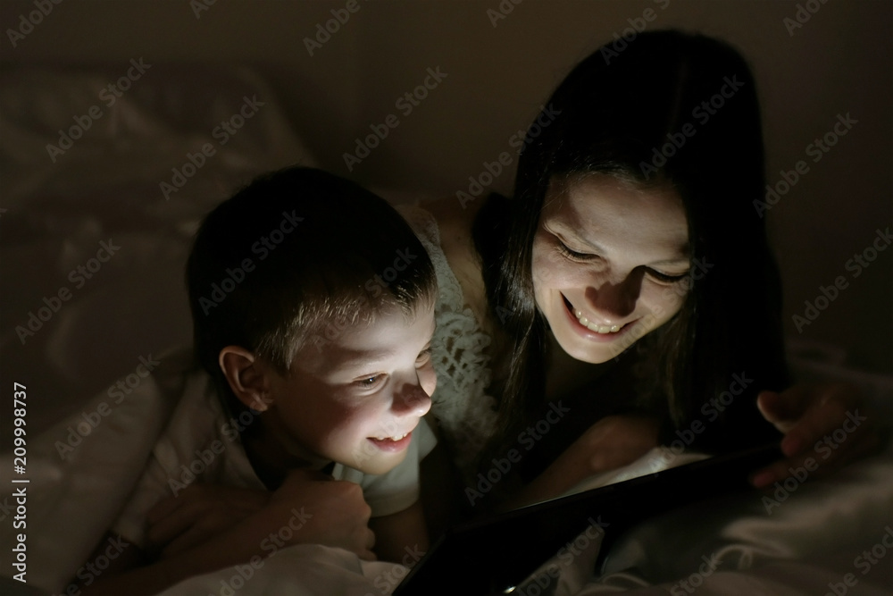 Young woman mom and her son watching a funny film together on tablet under the blanket. Young woman mom and her son watching a funny film together on tablet under the blanket.