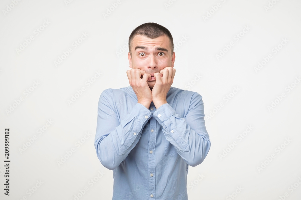 Portrait anxious young man in blue shirt biting his nails fingers freaking out. Portrait anxious young man in blue shirt biting his nails fingers freaking out.