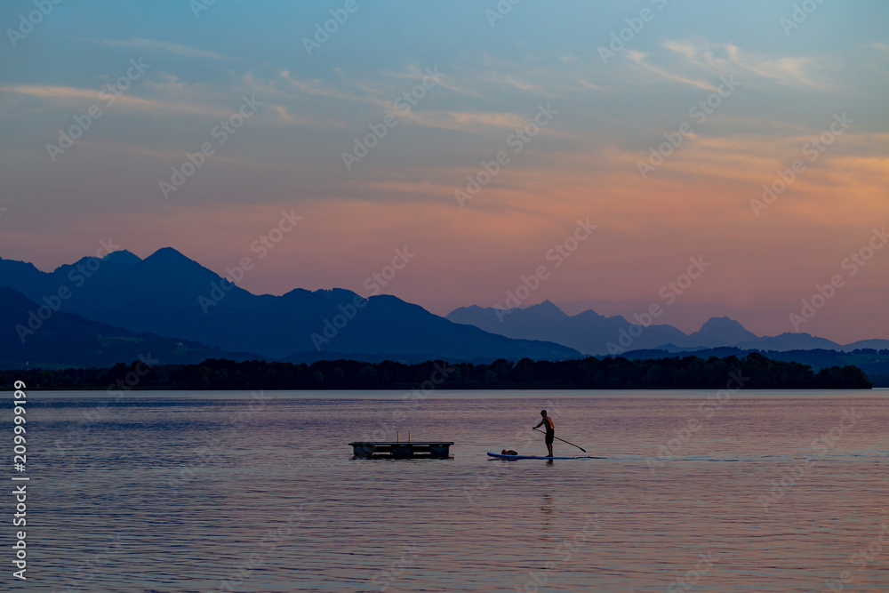 Silhouette of stand up paddle boarder paddling at sunset at Lake Chiemsee in Bavaria, Germany