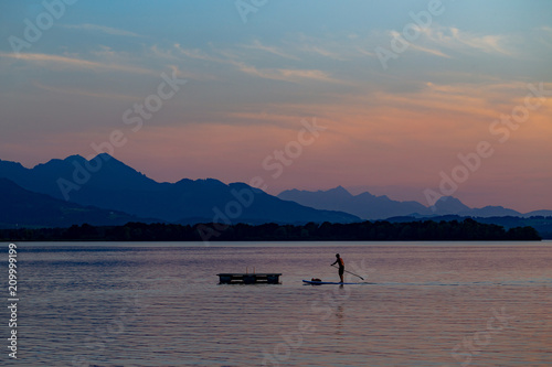 Silhouette of stand up paddle boarder paddling at sunset at Lake Chiemsee in Bavaria, Germany