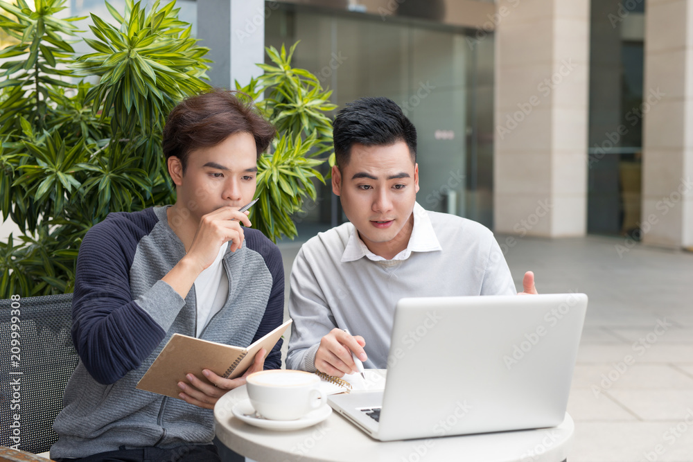 Two businessmen having a meeting in a classic coffee shop terrace, using a laptop computer. Two businessmen having a meeting in a classic coffee shop terrace, using a laptop computer.
