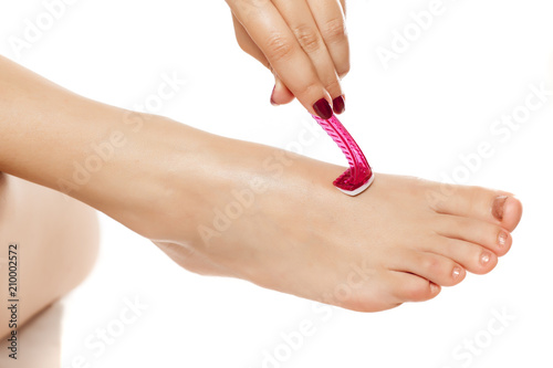 young woman shave the hairs on her feet with razor on white background