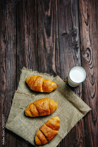 three croissants with glass of milk on rag and wooden table black background place for text, view from above