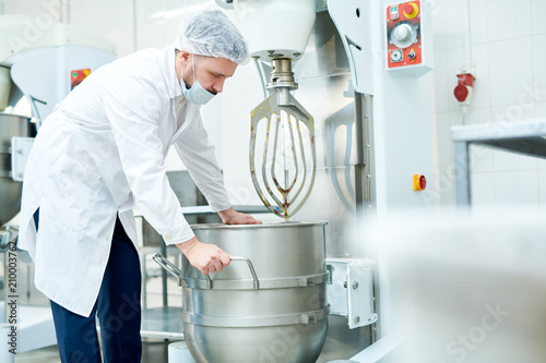 Confectionery factory worker in white coat operating dough mixing machine.  photo