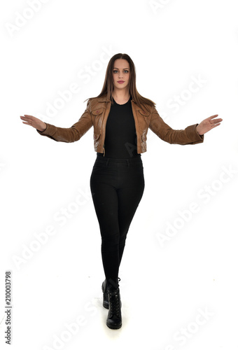 full length portrait of brunette girl wearing brown leather jacket. standing pose on white background.