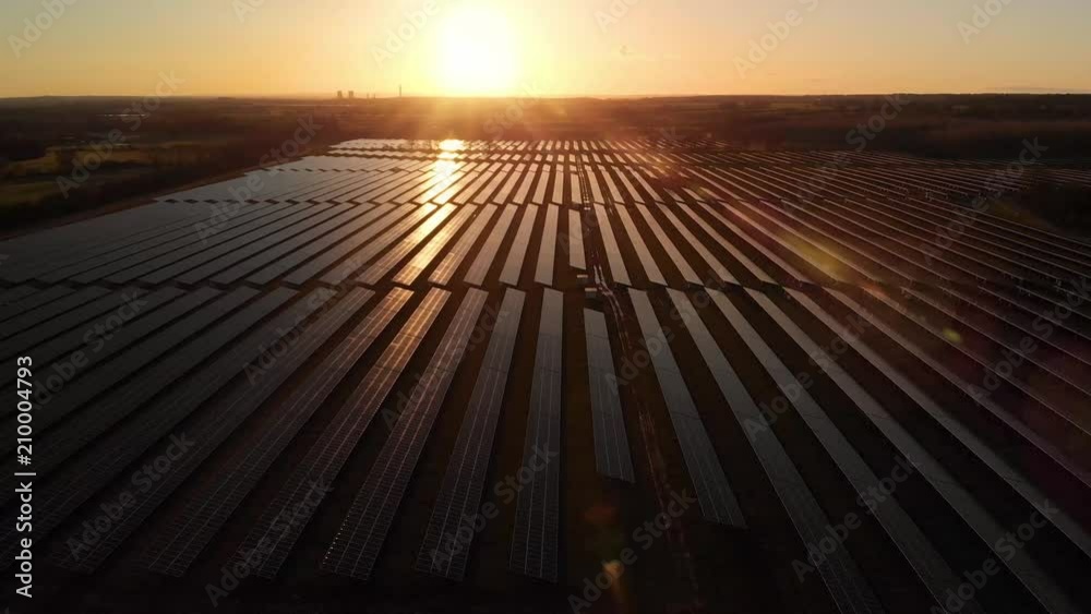 Sunrise over a modern electric solar farm with the sun glistening over the panels as the camera pans over them from the air