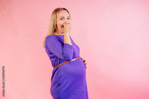 Beautiful blonde pregnant sleepy woman in a violet dress with big baby bump yawn and wants to sleep in the studio on a pink background