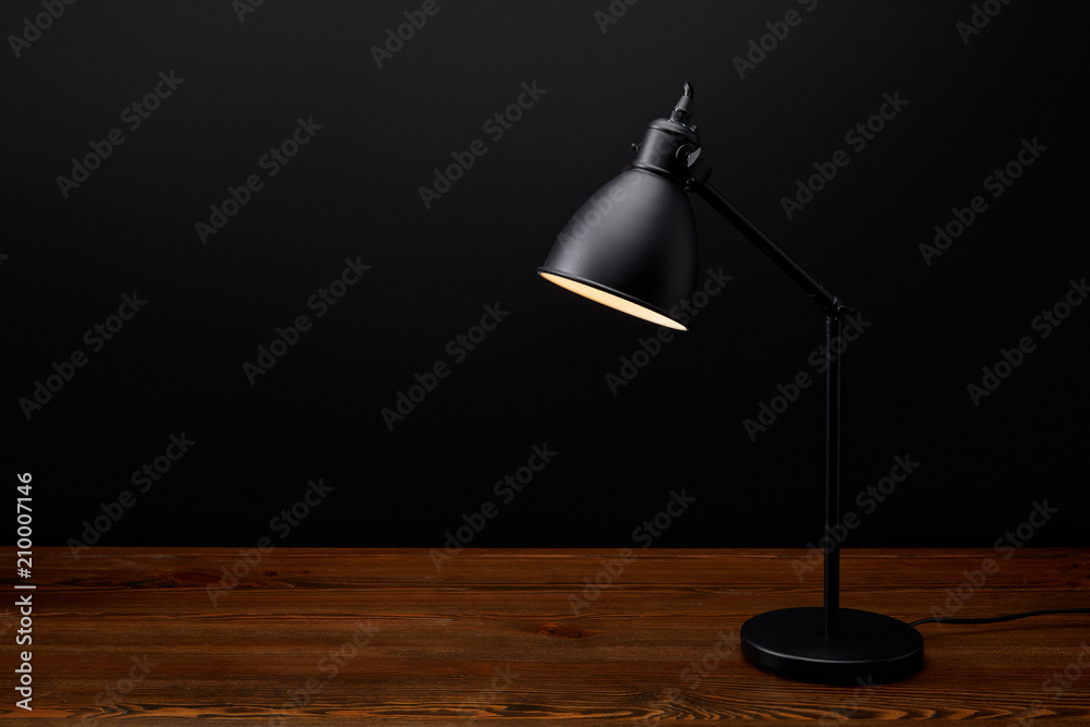 close up view of black lamp on wooden tabletop on black background close up view of black lamp on wooden tabletop on black background