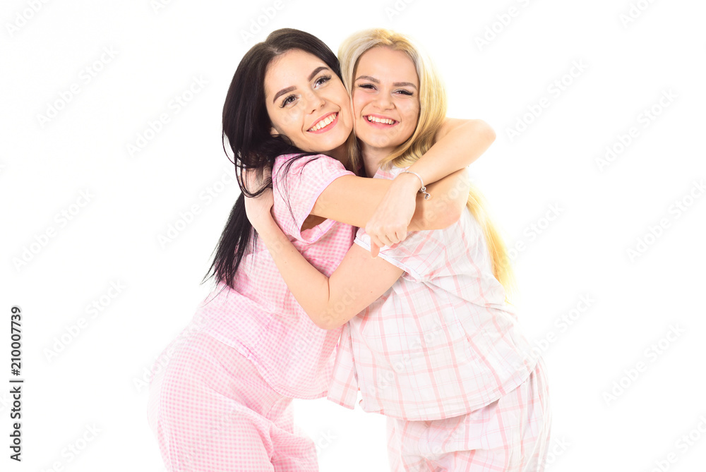 Sisters or best friends in pajamas. Blonde and brunette on smiling faces in clothes for sleep looks cute and friendly. Sisters best friends concept. Girls hugging tight, isolated on white background. Sisters or best friends in pajamas. Blonde and brunette on smiling faces in clothes for sleep looks cute and friendly. Sisters best friends concept. Girls hugging tight, isolated on white background.