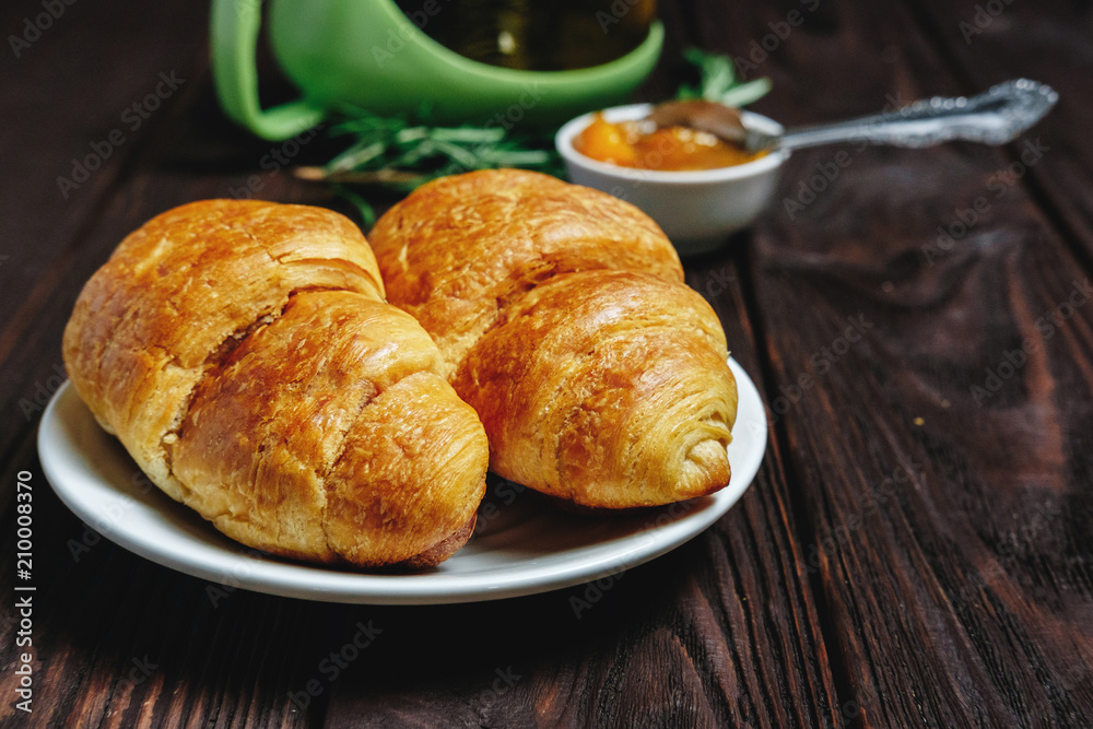 fresh croissants with jam on dark wooden table and tea with rosemary,