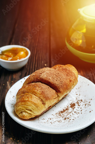 fresh croissants with jam on dark wooden table and tea with rosemary  sunshine  chocolate on food