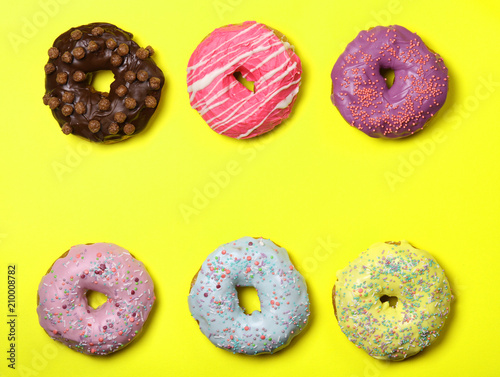 Many multicolored donuts on a yellow background. Frame, space for text