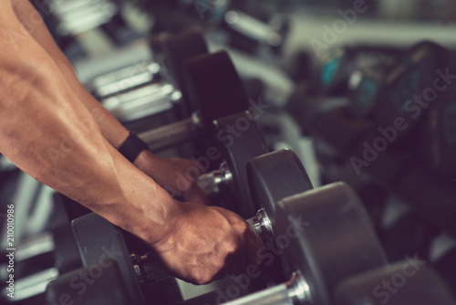 Close-up shot of sport man taking dumbbells from rack while having workout at modern gym