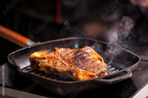 Concept of the correct cooking of meat. The chef prepares, fries a steak of mutton, pork or veal in a frying pan on an induction cooker, with the addition of spices, marinade and wine. Selective focus