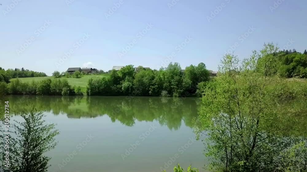 Aerial: Lifting off beside small lake wit beautiful green landscape arround it. Flying with drone and filming on beautiful sunny summer day. Aerial: Lifting off beside small lake wit beautiful green landscape arround it. Flying with drone and filming on beautiful sunny summer day.