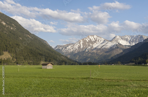 Green meadow with a lonly barn and in the background mountains with snow