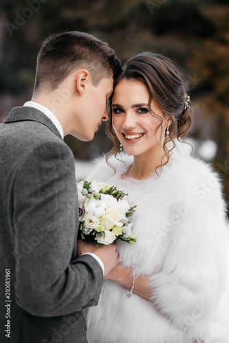 Loving and beautiful bride and groom stand in an embrace in the winter forest. Vertical frame