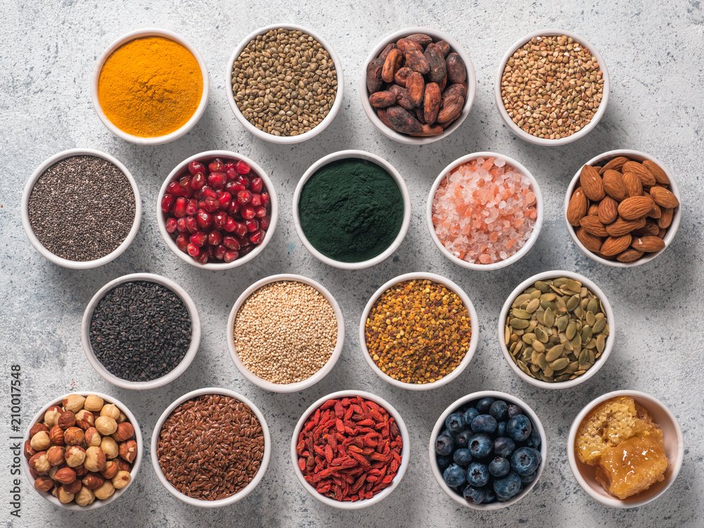 Various superfoods in smal bowl gray concrete background. Superfood as chia, spirulina, raw cocoa bean, goji, hemp, quinoa, bee pollen, black sesame, turmeric. Top view or flat-lay.