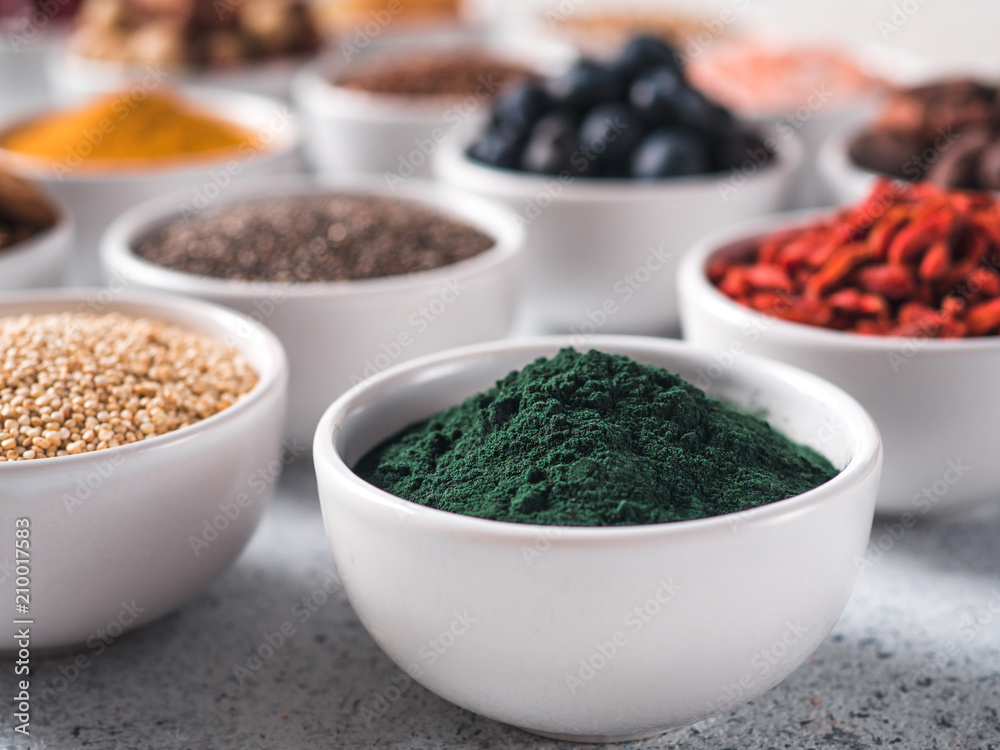 Spirulina powder in small white bowl and other superfoods on background. Selective focus. Different superfoods ingredients. Concept and illustration for superfood and detox food Spirulina powder in small white bowl and other superfoods on background. Selective focus. Different superfoods ingredients. Concept and illustration for superfood and detox food