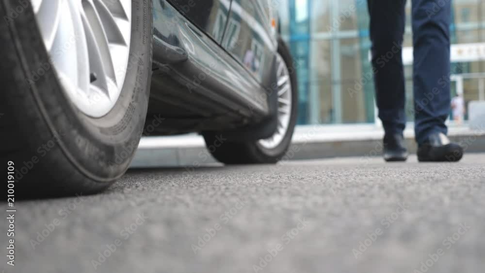 Legs of girl getting out of auto. Business man opens and holds the car door for the beautiful young woman in high heels shoes. Chauffeur opening door of automobile for female passenger. Close up