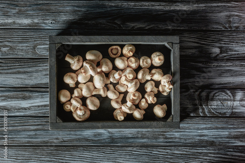 top view of uncooked champignon mushrooms in box on grey wooden surface