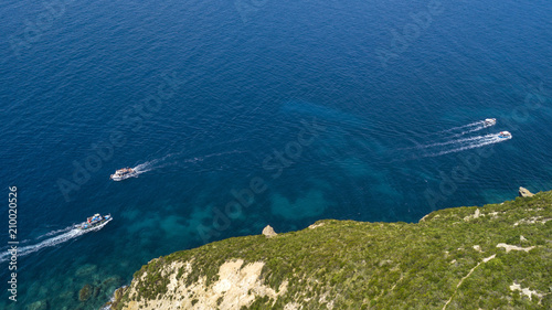 Aerial view of four white motorboats running on the azure waters of the Tyrrhenian Sea. On his trip near the coast the boat leaves a white trail in the waves of the sea.