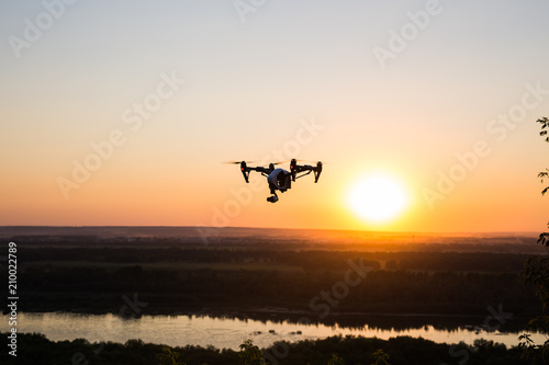 silhouette of drone, quadrocopter with photo camera flying in the sky. © satura_