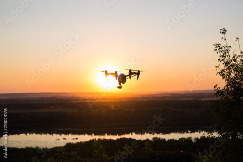 silhouette of drone, quadrocopter with photo camera flying in the sky. © satura_