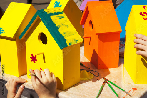 Children painting birdhouses bright colors of orange and yellow. Kids woodcraft lesson, making wooden houses for birds