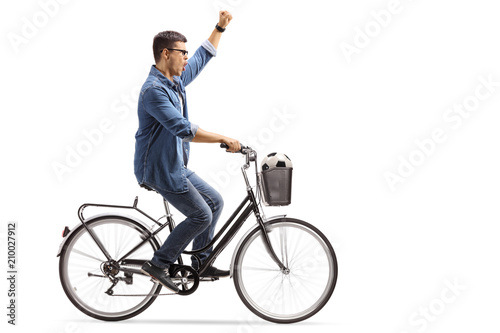 Young guy with a football riding a bike and gesturing happiness