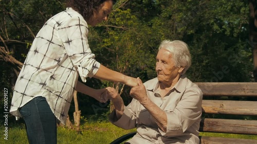 Help the elderly. The daughter helps the elderly mother to get up from the bench.