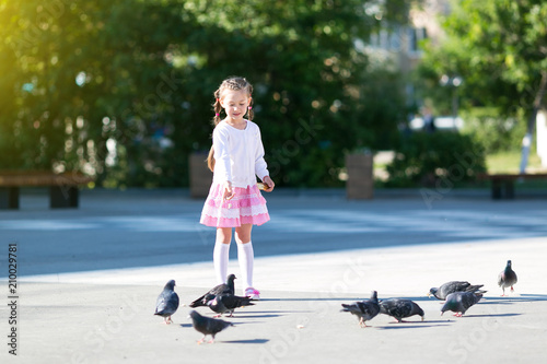 A little girl feeds pigeons. Beautiful girl gives bread to the birds on the city street.