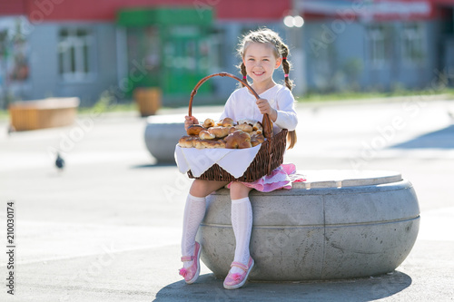 Little girl with a basket of bread. The girl holds a basket full of bread, rolls and flour products.