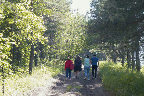 Group of young people walking on the forest path at sunny day