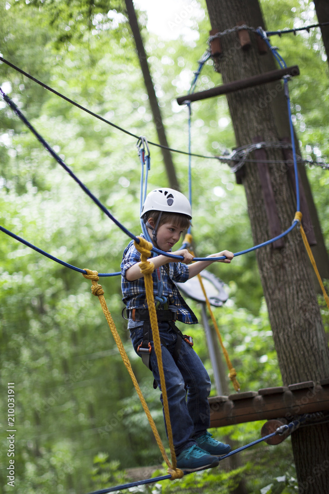 boy enjoys climbing in the ropes course adventure. smiling child engaged climbing high wire park. boy enjoys climbing in the ropes course adventure. smiling child engaged climbing high wire park.