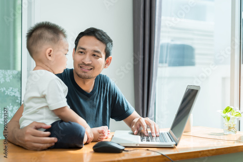 Asian father and little son typing someting on laptop computer on workplace at office home happiness laughing together, happy family concept.