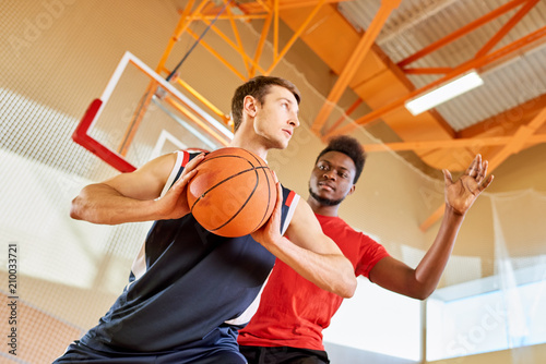 Young black man trying to stop contender from shooting goal while playing basketball together in gym. © Seventyfour