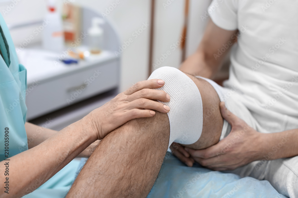 Orthopedist bandaging patient's leg in hospital Orthopedist bandaging patient's leg in hospital