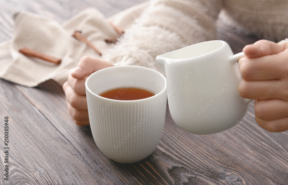 Woman pouring milk into cup of tea on table Woman pouring milk into cup of tea on table