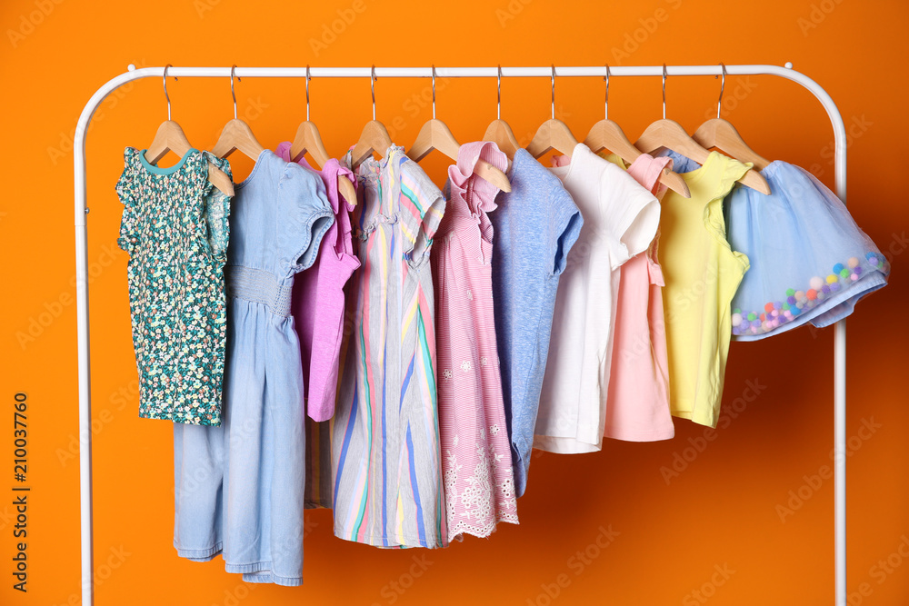 Rack with stylish child clothes on color background