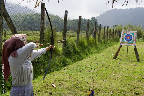 Young woman is aiming in archery  practice n the field with a target in front of her. photo