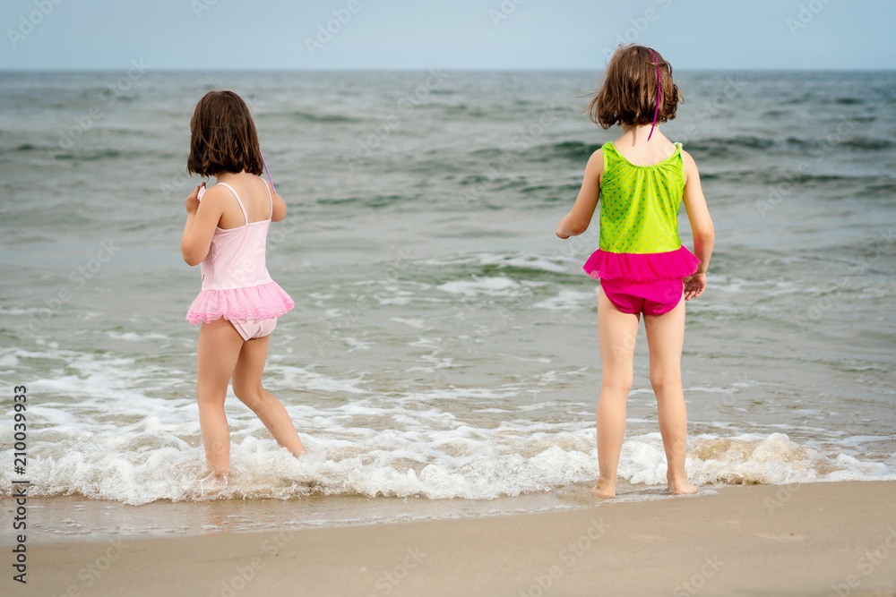 two little girls sisters are standing and playing on the sand at the beach on a summer day