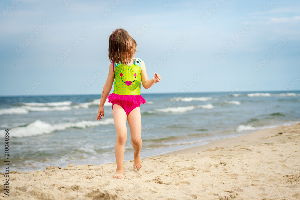 little girl is walking on the sand on the beach with a shell in her hand in the summer