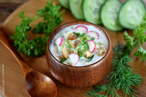 Cold soup Tarator with kefir, cucumber and radish in a wooden bowl. Bulgarian cuisine meal